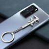A silver metal jewelry measuring ruler and caliper keychain attached to a chain, placed on a smartphone.