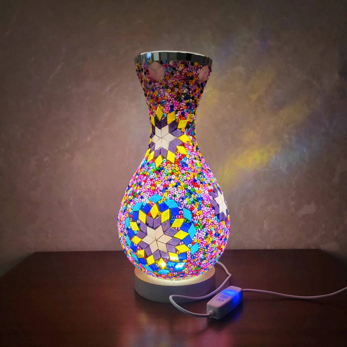 Lámpara de mesa de vidrio colorida con diseño texturizado tipo mosaico sobre una superficie de madera.