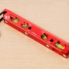 A red magnetic level ruler with measurement markings and several green magnetic levels is shown on a wooden surface.