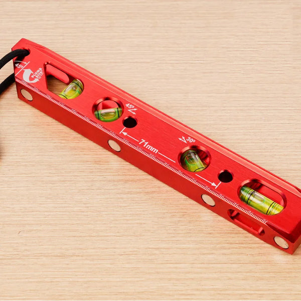 A red magnetic level ruler with measurement markings and several green magnetic levels is shown on a wooden surface.