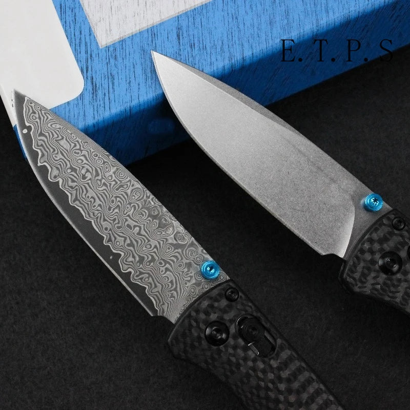 A silver Damascus steel folding pocket knife with a black textured handle is shown next to its blue blade collar and a blue b