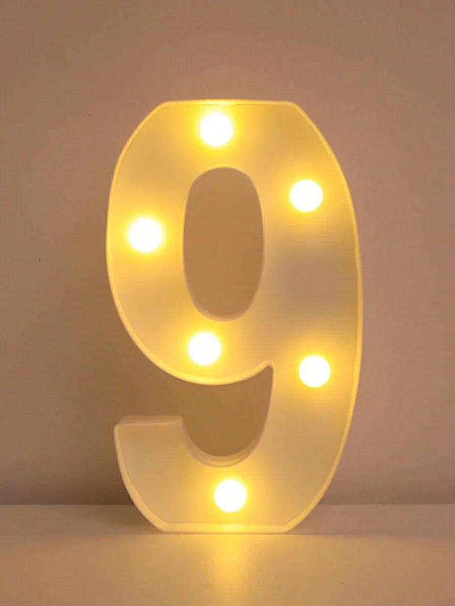 Una luz nocturna de letra y número LED brillante con forma de 9, iluminando la superficie con luz amarilla cálida.