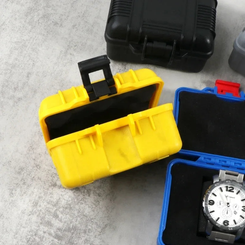A yellow watch storage case is open, revealing a black watch inside, next to a black storage box and an open blue watch case.