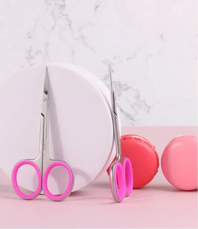 A pair of professional stainless steel nail cuticle trimmers with pink handles resting on a white plate.