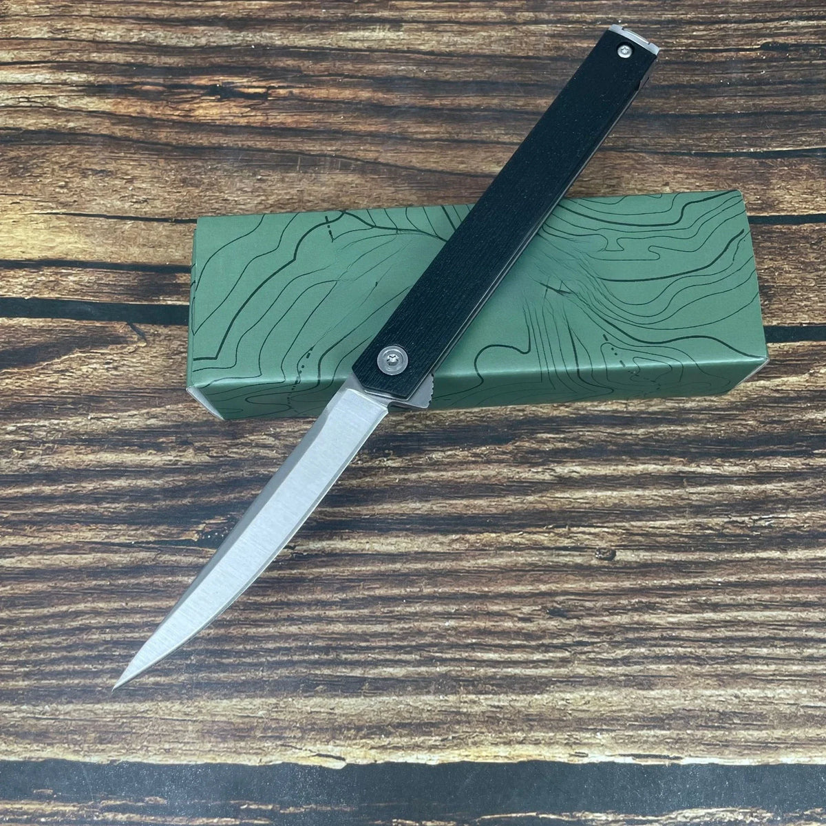 A folding utility knife with a black handle and silver blade rests on a green wooden box.