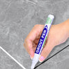 Une main tient un stylo à coudre violet marquant une ligne sur une surface de carreaux gris.
