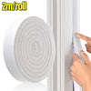A hand is applying a roll of thick foam window sealing strips onto a white window frame.