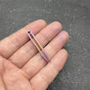 A hand holds a titanium clip tweezers with a pinkish-purple tint against a dark gray background.