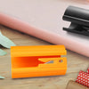 Orange sliding wrapping paper cutter and black cutter shown on a wooden surface with floral greenery.