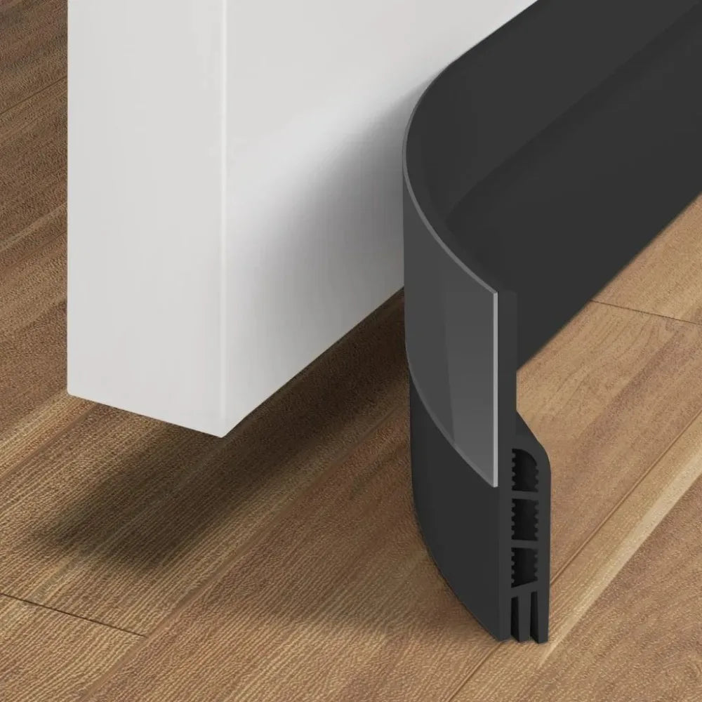 A black door draft stopper with a flexible seal is shown against a white wall and wooden floor.