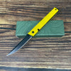A yellow foldable utility knife with a black blade rests on a wooden surface next to a green box.