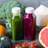 A collection of fresh juices and ingredients including green juice, purple juice, citrus fruit, avocado, and tomatoes.