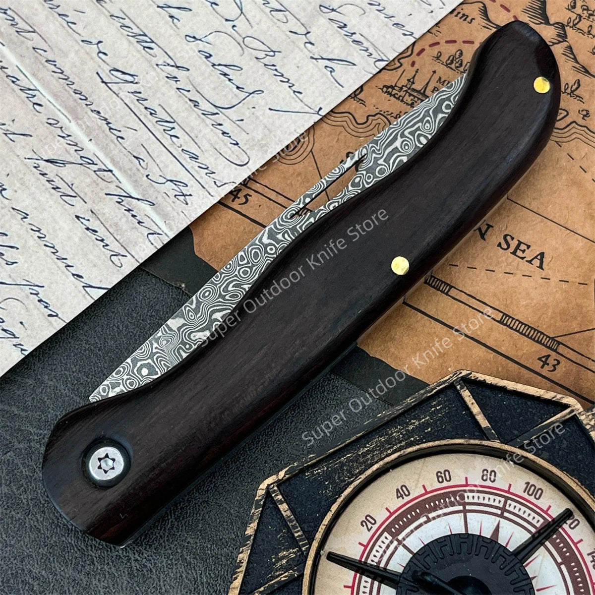 A folding knife with a dark ebony handle and Damascus steel blade rests on aged paper.