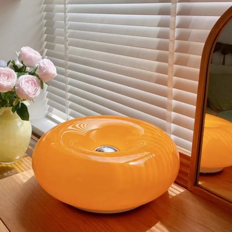Orangefarbener runder dekorativer LED-Wandleuchter mit Donut-Design auf Holzoberfläche neben rosa Rosen