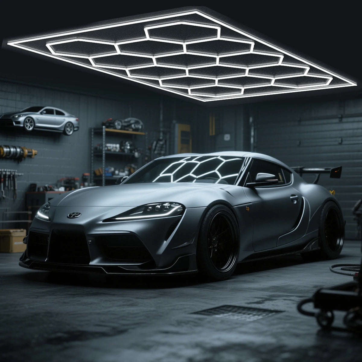A silver sports car is parked under a hexagonal LED ceiling light fixture in a dark garage setting.