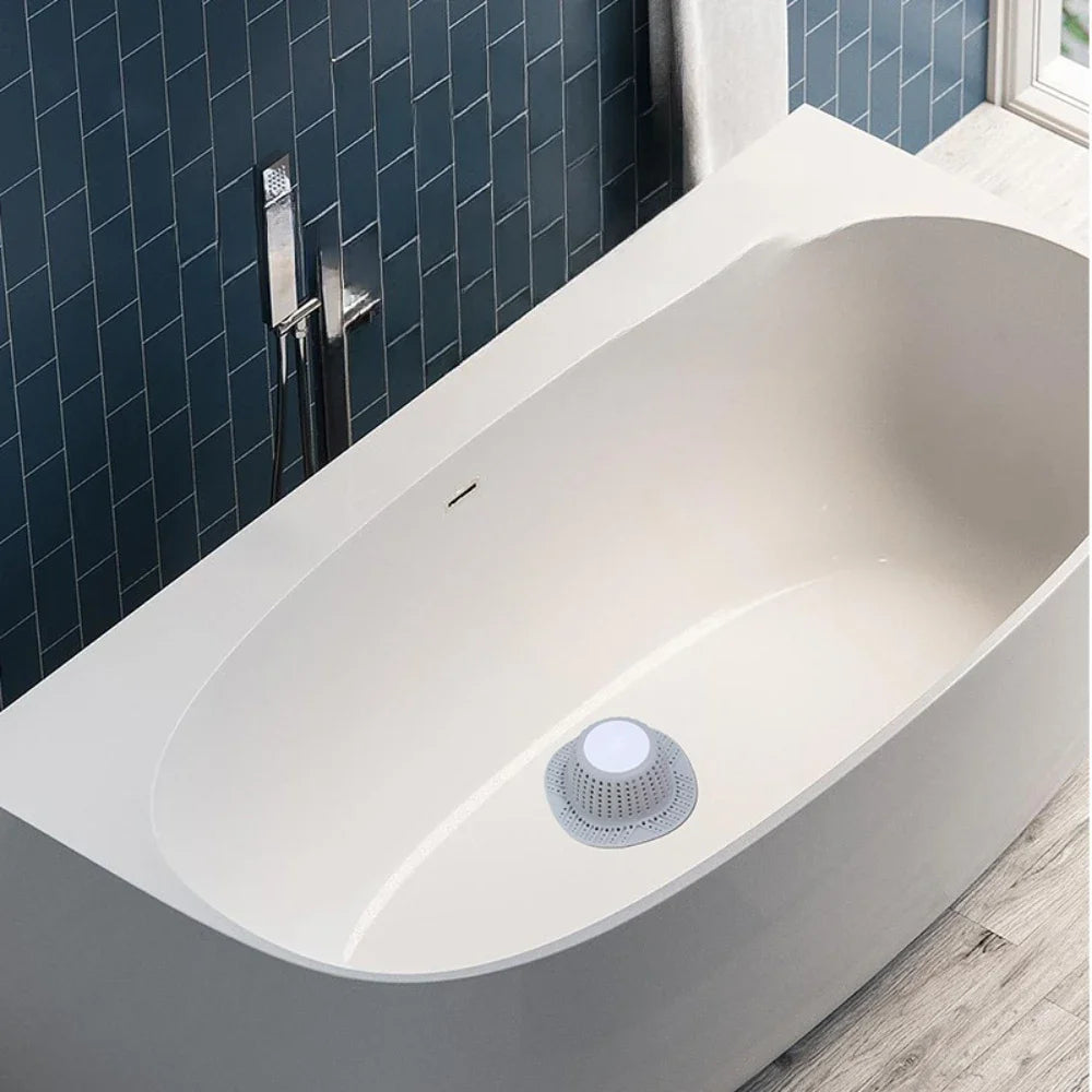A white, oval bathtub with a visible drain protector installed on the side against a dark blue tiled wall.