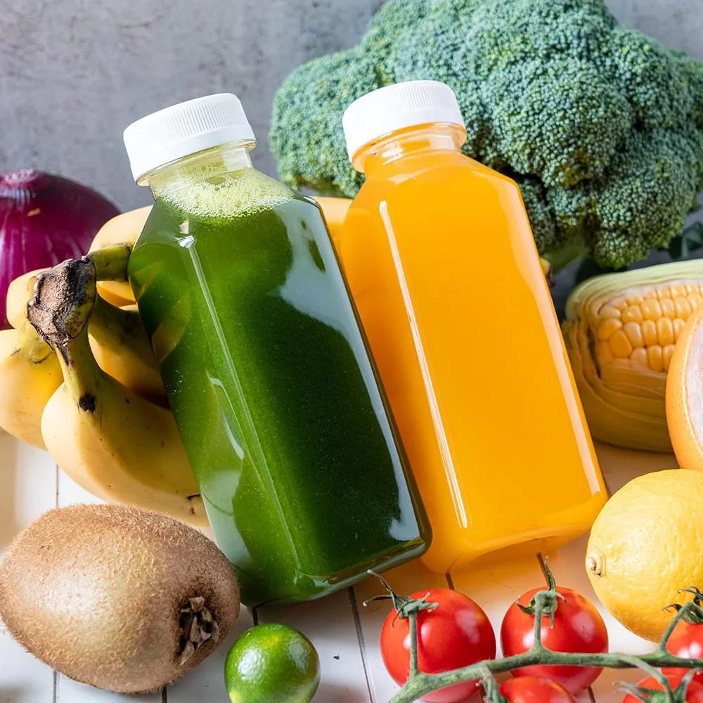 A collection of fresh fruit and vegetables arranged around green and orange juice bottles.