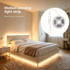 Una tira de luz sensible al movimiento ilumina un dormitorio moderno, resaltando la cama y el área circundante.