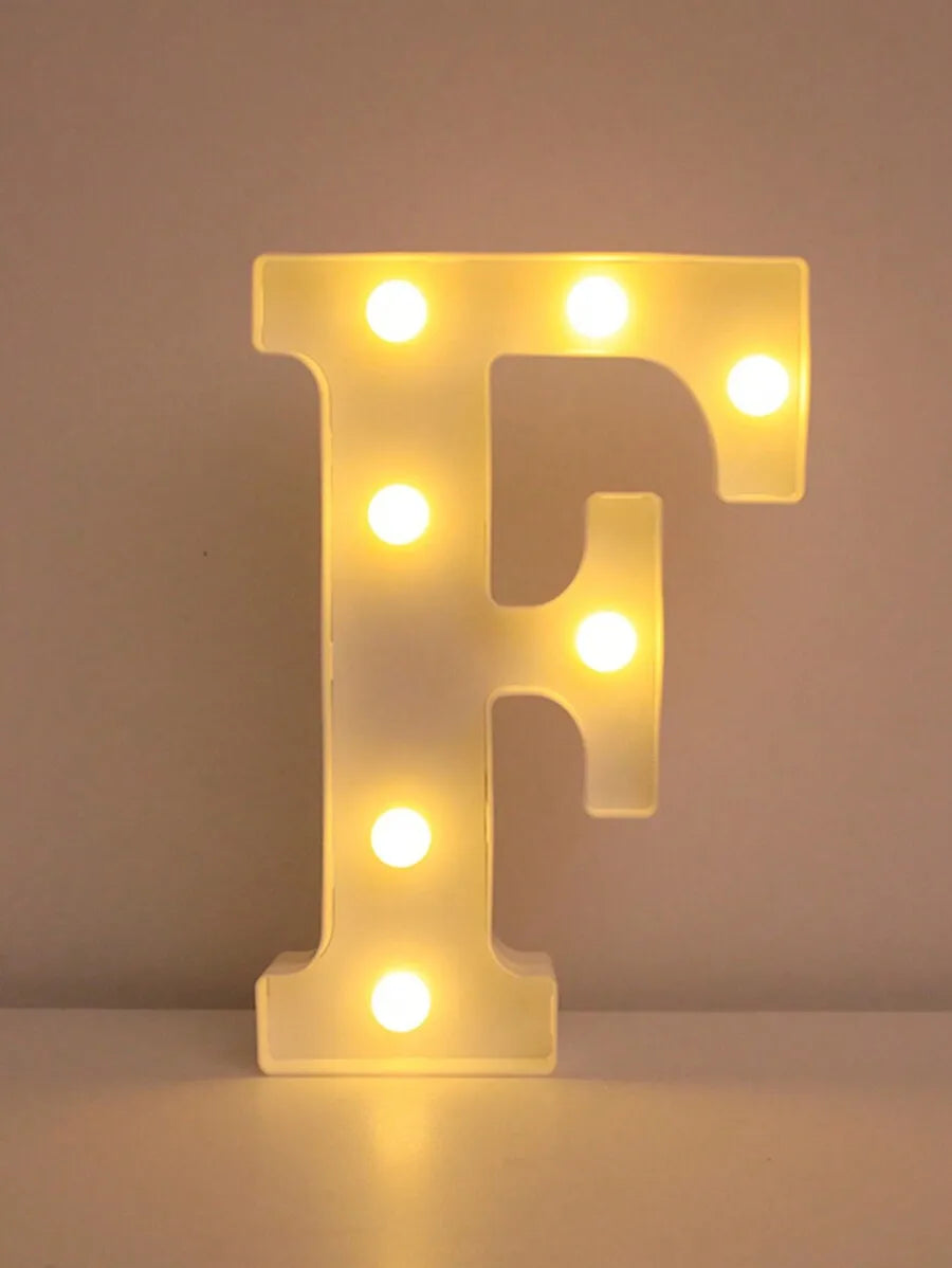 Luz nocturna de letra F amarilla brillante LED montada en una superficie blanca.