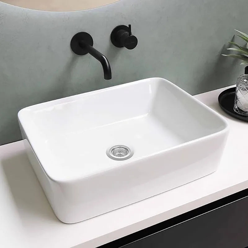 Lavabo de cerámica blanca con rejilla de desagüe metálica montado en una pared gris claro.