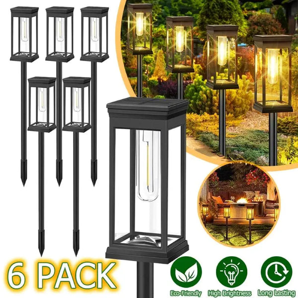A pack of six black solar path lights with glass enclosures shown against a blurred outdoor landscape.