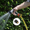 A hand sprays water from a 3/4 inch aluminum garden hose quick connector onto green foliage.