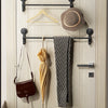 A wooden towel rack with a black metal bar holds a brown hat and a gray towel, alongside a brown leather purse.