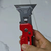 A hand holds a red utility knife with a silver folding blade against a light background.