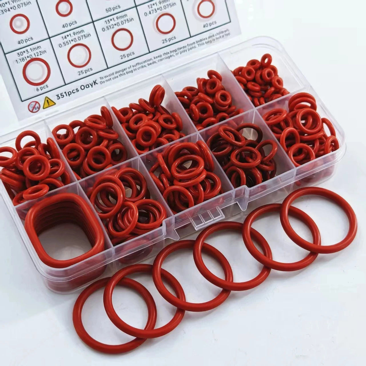 A clear plastic container holds a set of multi-size silicone O-rings in various shades of red and orange.