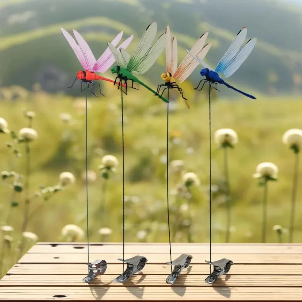 Five colorful simulation dragonfly clips suspended from thin wires on a wooden surface against a blurred green field backgrou