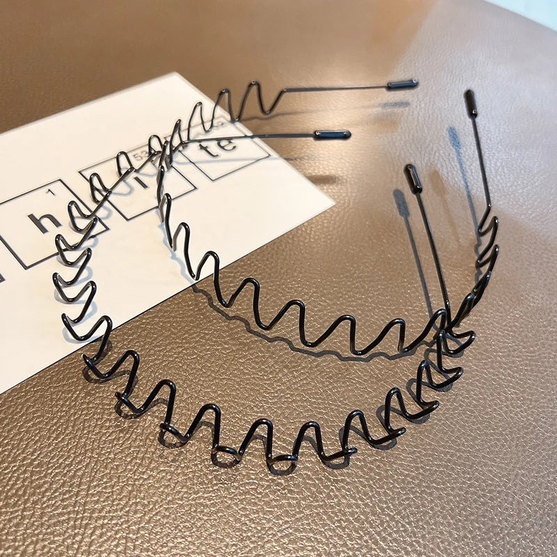 A close-up of black metal elastic headbands with wavy designs laid out on a brown surface.