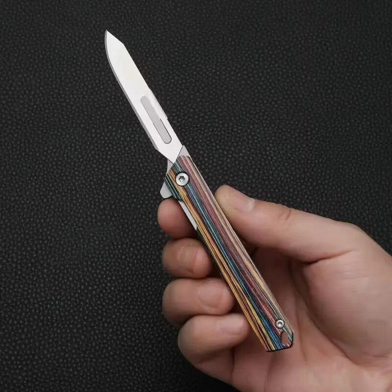 A hand holds a portable utility folding knife with a silver blade and multicolored handle against a dark background.