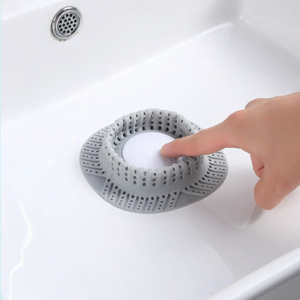 A hand is placing a silicone hair catcher drain protector into a white bathtub drain.