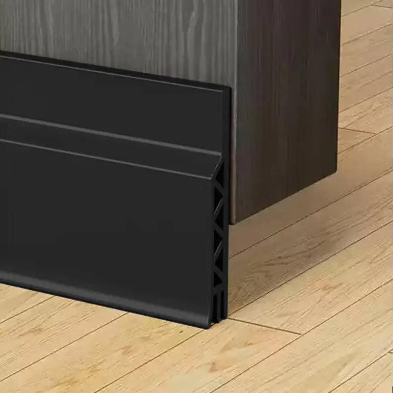 A black door draft stopper weather stripping seal installed on a wooden door frame.