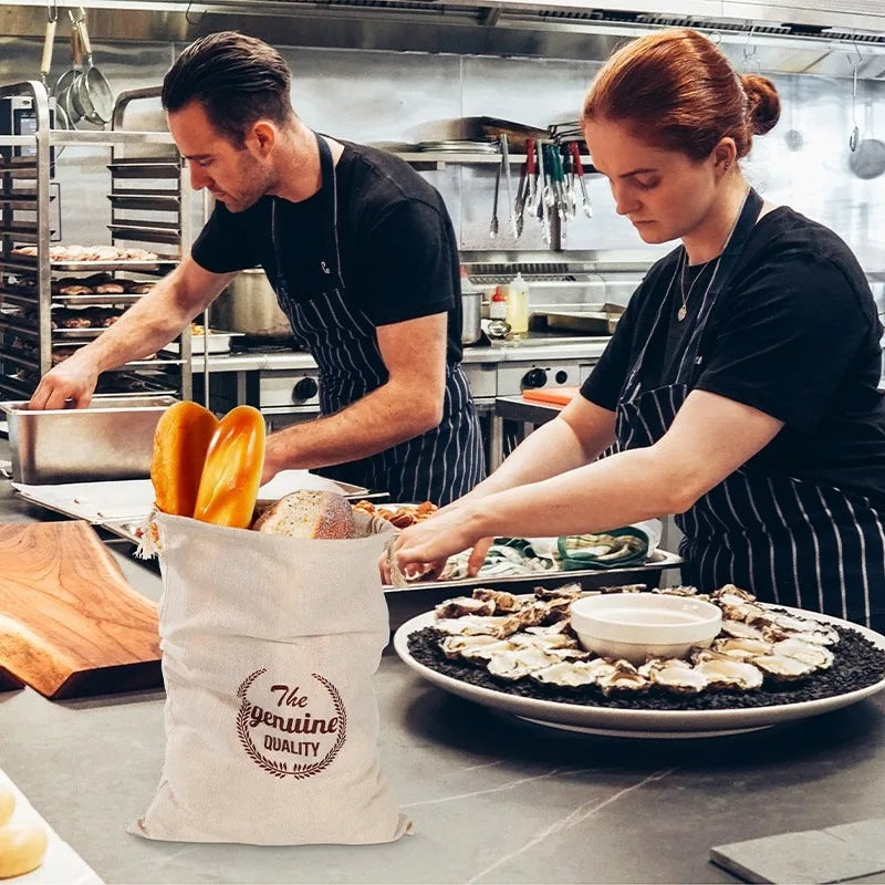 A woman in a black shirt and striped apron is preparing food on a stainless steel counter, with a linen drawstring bag in the