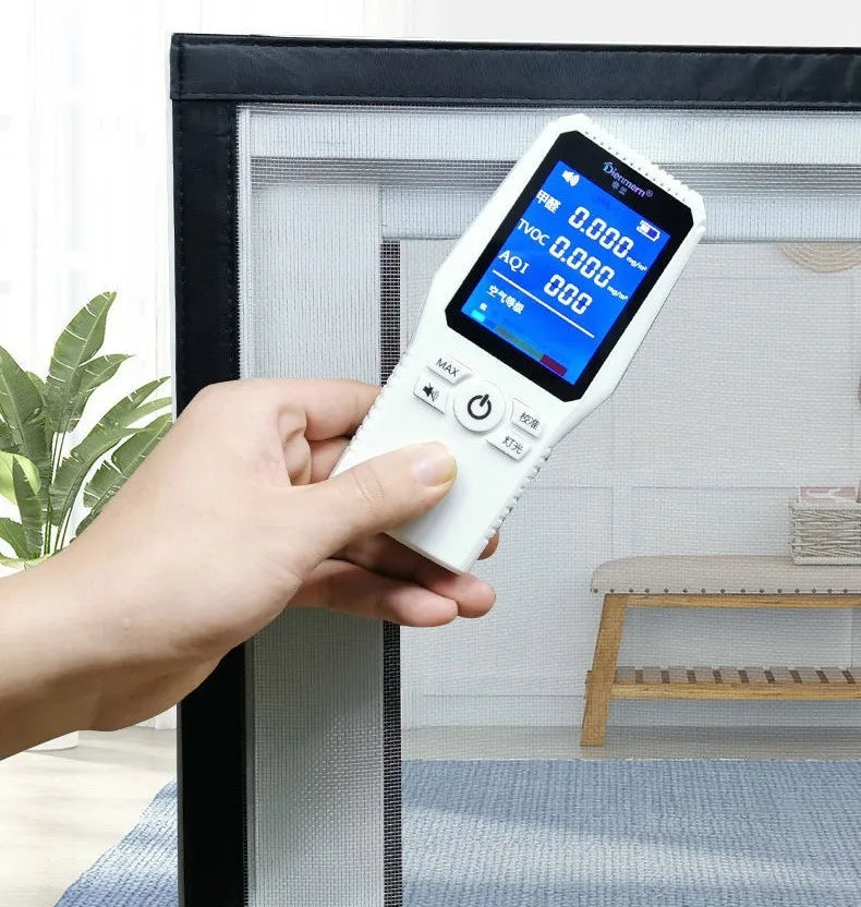 A hand holds a digital electronic device with a screen displaying 0.000 and buttons, positioned in front of a window frame.