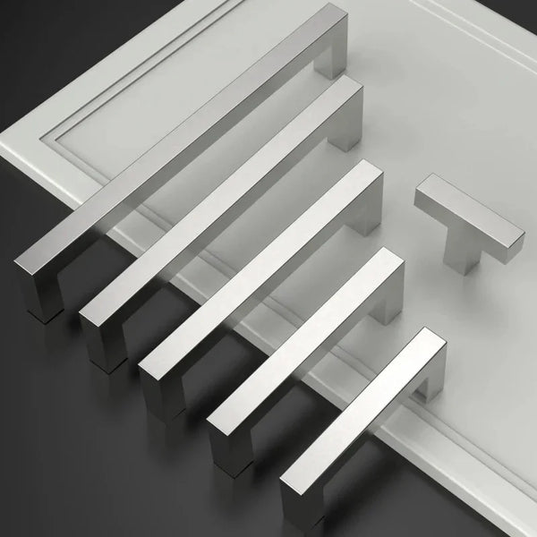 A set of modern stainless steel cabinet and drawer pulls arranged diagonally on a light gray surface.
