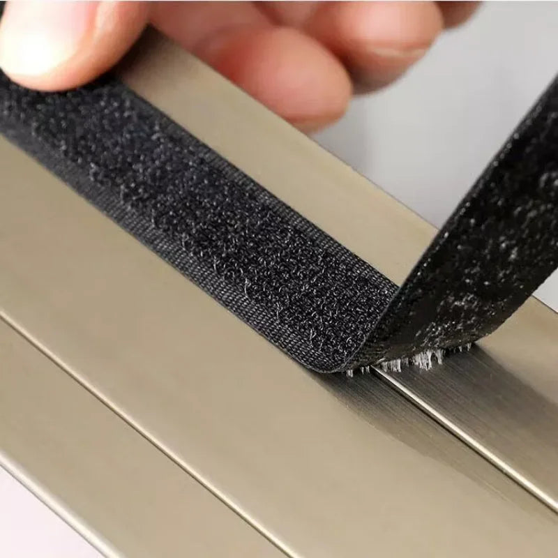 A hand is pulling a black self-adhesive window mosquito net across a metal frame.