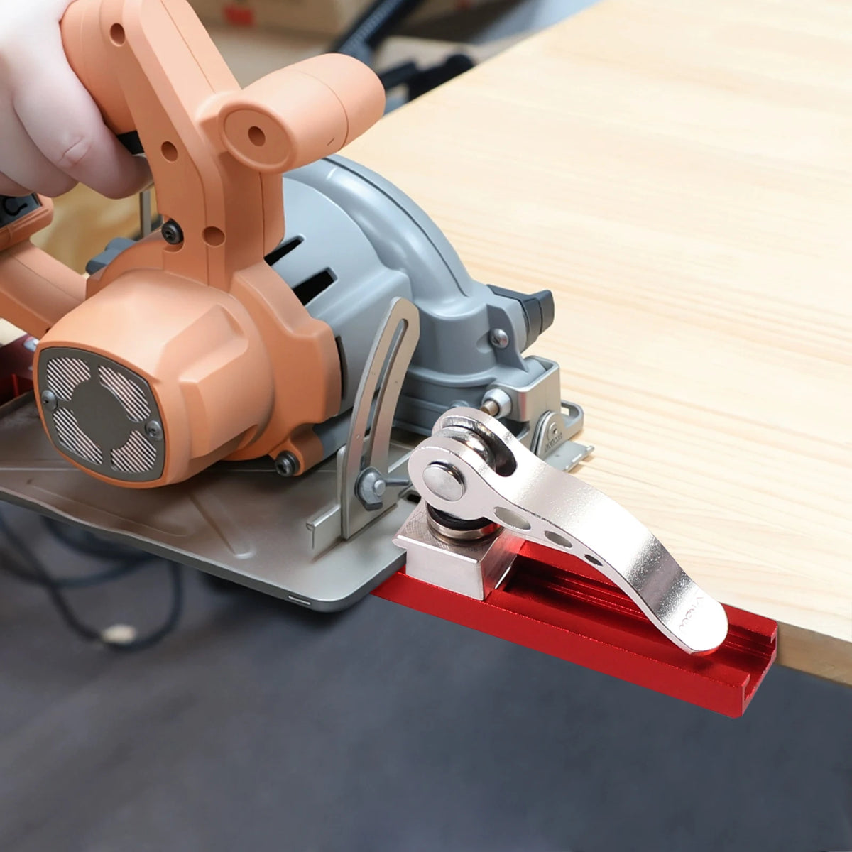 A hand is holding an orange guide rail component of a precision adjustable circular saw, resting on a wooden surface.