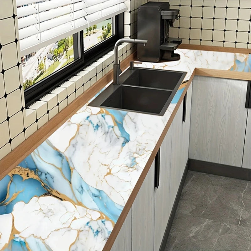 A kitchen countertop featuring white marble with blue and gold veining, a stainless steel sink, and light wood cabinetry.