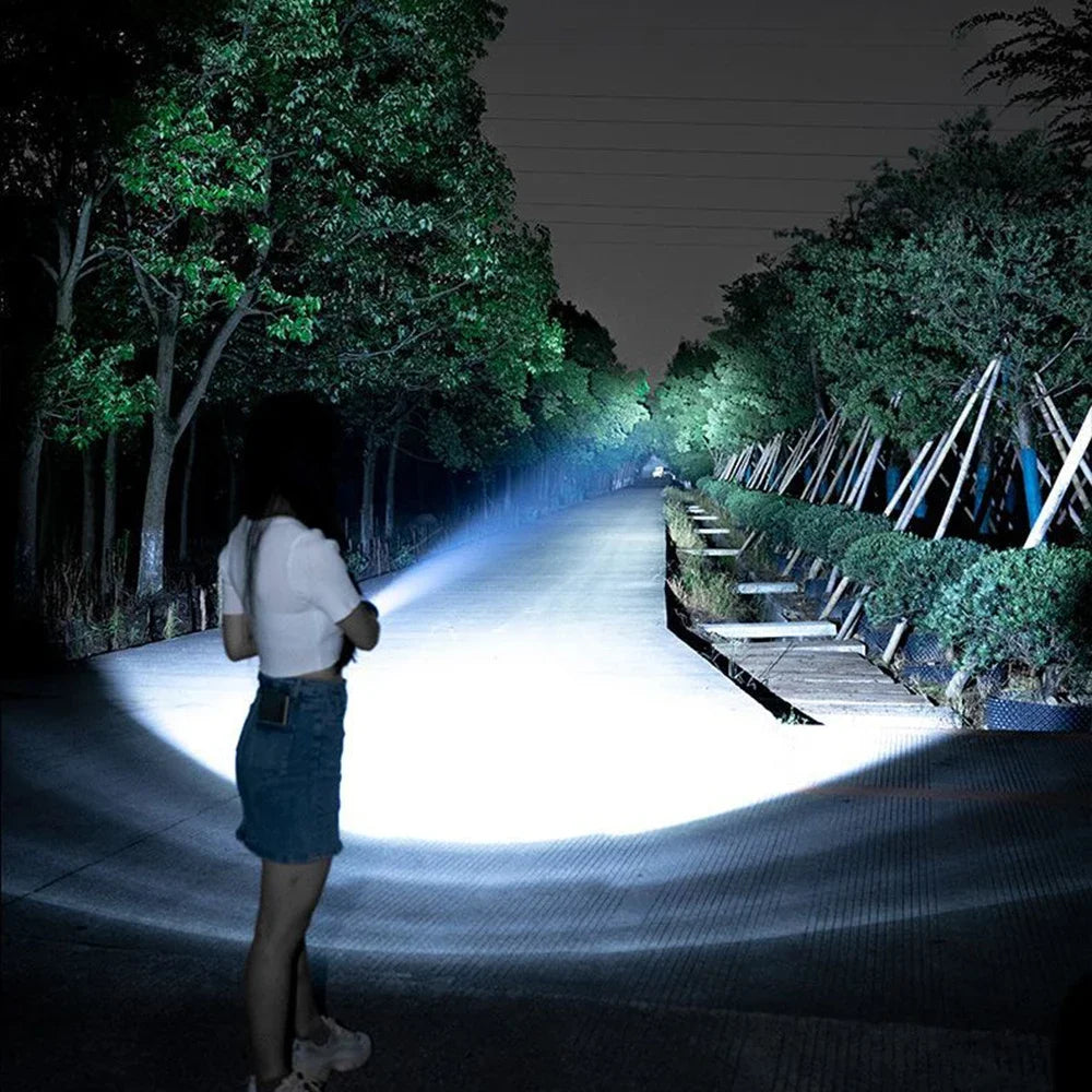 A person is walking down a paved path illuminated by a bright, focused beam from a high-power tactical LED flashlight.