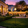 A golden crescent moon shaped solar pathway light with an owl design illuminates a garden path at dusk.