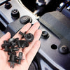 Une main tient plusieurs clips de fixation pour carrosserie et pare-chocs.