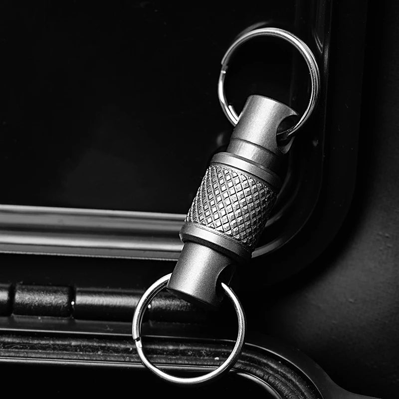 A close-up shot of a titanium alloy rotating keychain key holder attached to a dark surface.