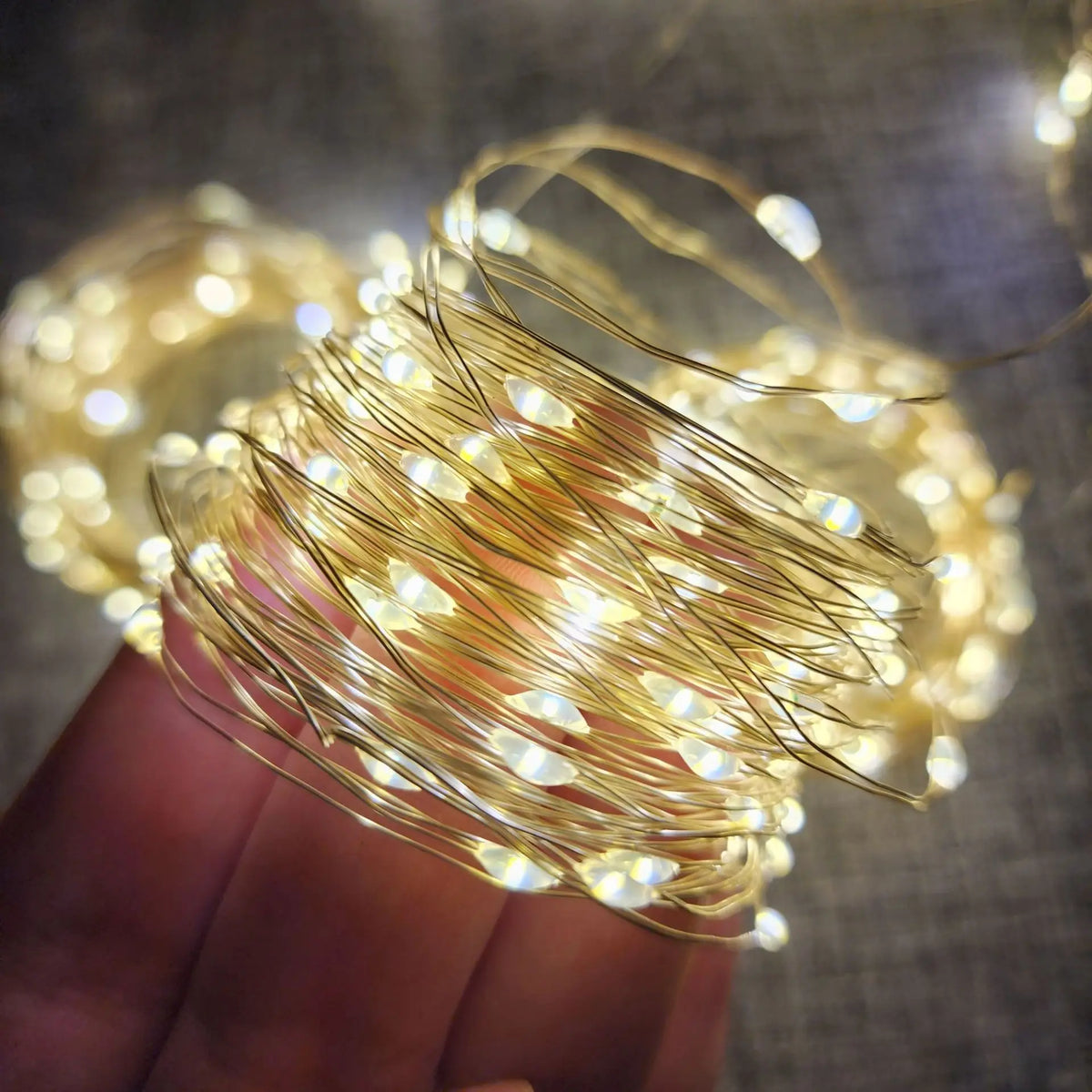 Une main tient un faisceau de guirlandes lumineuses en fil de cuivre blanc chaud avec de petites ampoules LED.