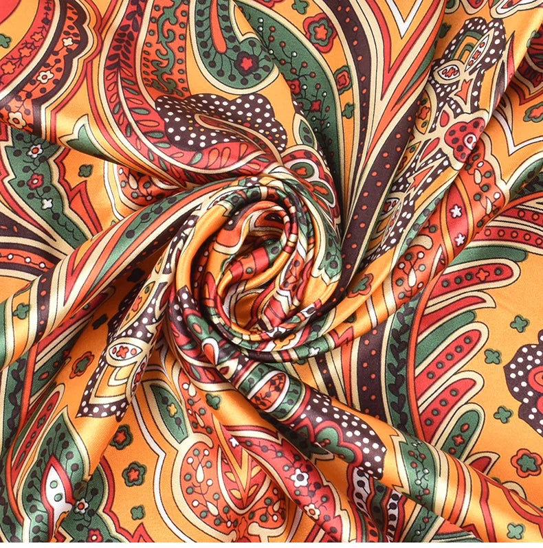 Gros plan d'un foulard hijab en soie satinée carrée avec un motif paisley orange, vert et brun complexe.