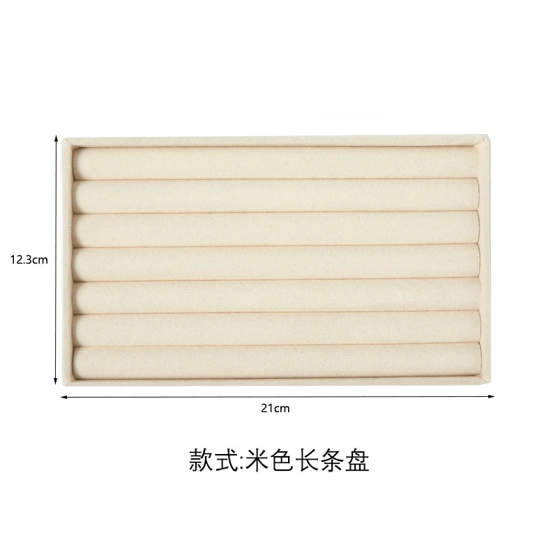 A rectangular storage tray for jewelry made of beige plush velvet with multiple horizontal slots.
