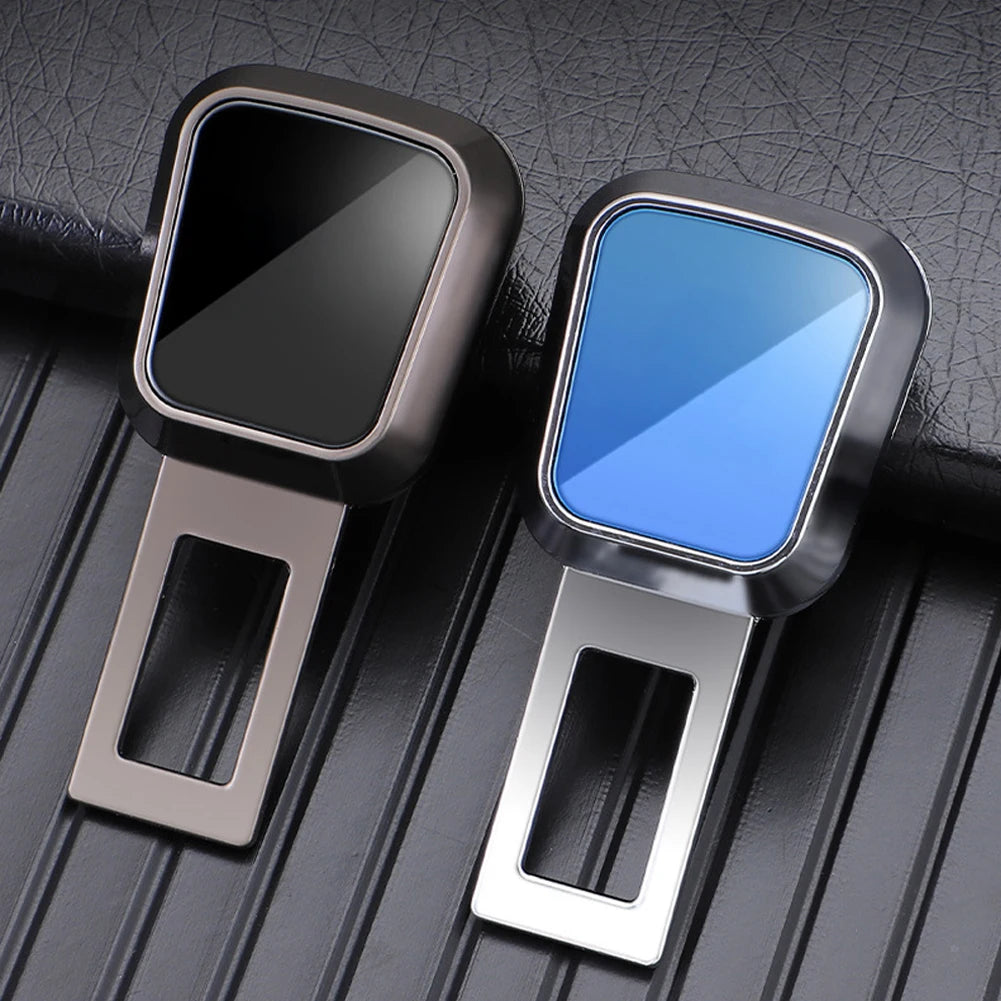 A pair of silver seatbelt clip extenders, one black and one blue, displayed on a dark leather surface.