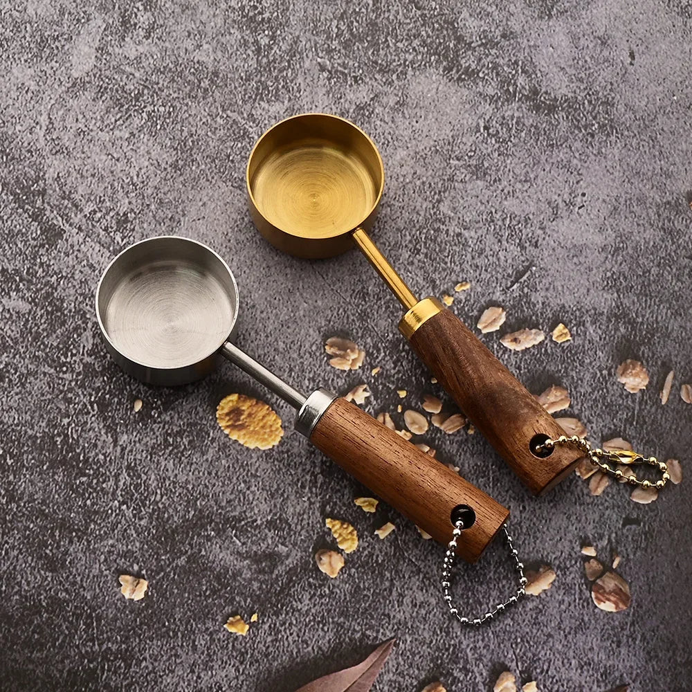 A set of stainless steel and wooden measuring spoons resting on a dark gray surface with scattered dried plant material.