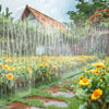 A multi-directional soaker hose is watering a garden with yellow flowers and greenery.
